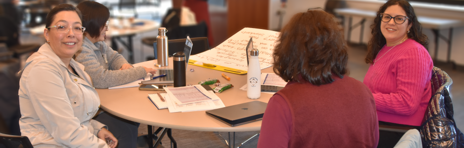 Four women participants around a round table at the 12/12/25 New Directors' Orientation. Two are looking at the camera.