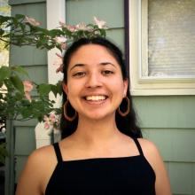 A photo of Elena standing with a house and tree branches in the background